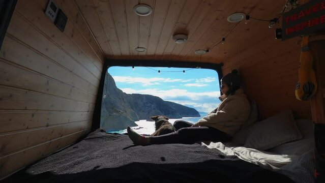 Woman sit on the back of a camper van with dog looking at Porto Katsiki beach in Lefkada island, in Greece