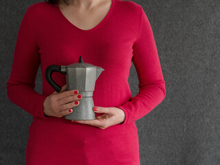 Close-up of a coffee maker held in the hands of a woman dressed in red against a grey background
