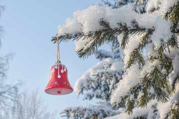 A red Christmas tree toy bell hangs on a snow-covered spruce branch in the forest after a heavy snowfall. Snow covering a pine tree in the forest. Beautiful winter landscape. Snow fairy tale