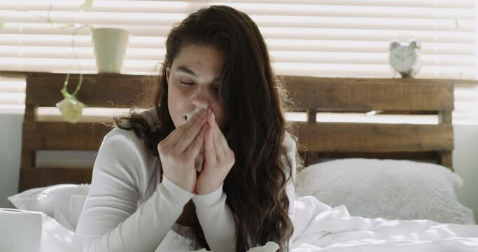 Blowing nose, tired or sick woman in bedroom or house with flu virus, cold crisis or health problem. Sneeze, sinus or exhausted person with tissue toilet paper, fever or allergy illness in home