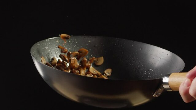 Chef cooking mushrooms on wok frying pan close up. Champignons mushroom with salt in pan. Restaurant Food concept