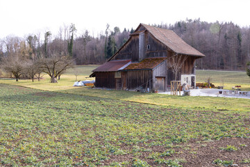 Old wooden barns on a green meadow, benches and tables in front of the house, ideal for photo compositions, during the day, cloudy sky without people