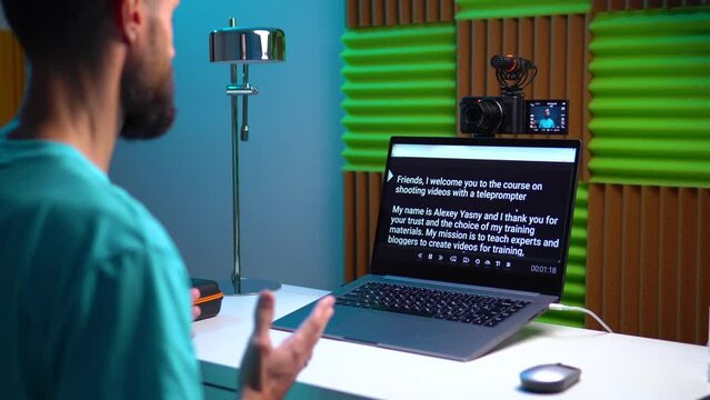 A young man shoots a video on a camera while reading text from a teleprompter on a laptop