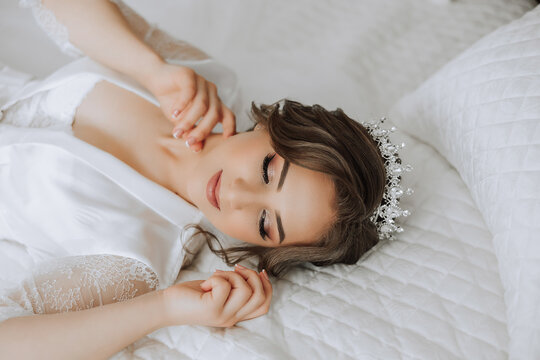 A beautiful brunette bride with a tiara in her hair is getting ready for the wedding in a beautiful robe in boudoir style. Close-up wedding portrait, photo.