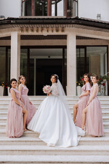 Group portrait of the bride and bridesmaids. Bride in a wedding dress and bridesmaids in pink or powder dresses and holding stylish bouquets on the wedding day.