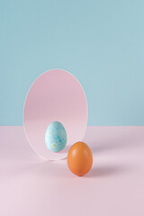 Creative Easter concept with egg and mirror on pastel pink and blue background. Minimal Easter holiday idea.