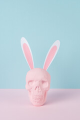 Skull with rabbit or bunny ears on pastel blue background. Creative minimal Easter concept.