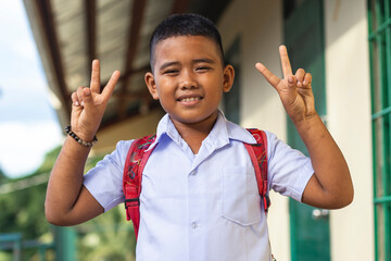 A poor but happy rural school kid makes peace signs with both hands. Outside a simple small classroom building.