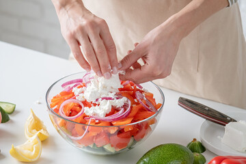 Woman adding feta cheese to bowl of Greek salad