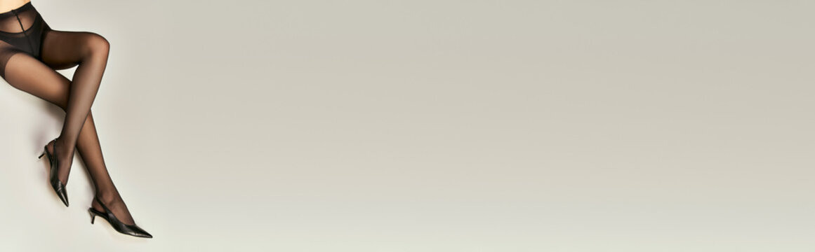 hosiery banner, cropped shot of young model in black shoes and pantyhose sitting on grey background
