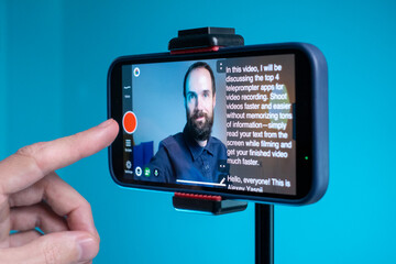 A young man shoots a video on a smartphone while reading text from a teleprompter on a screen