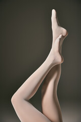 cropped view of young model in sheer white pantyhose posing with raised legs on dark grey background