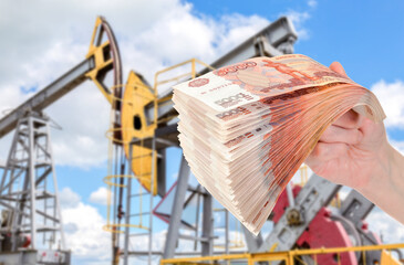 Russian roubles in the hand against the oil pump jack fracking crude extraction machine - 696424156