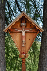 Wayside shrine with jesus statue on crucifix between trees, Italy