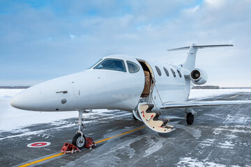 Modern white corporate jet plane with an opened gangway door at the winter airport apron