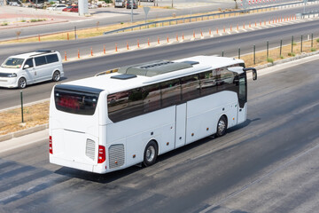White modern comfortable tourist bus driving through by suburban highway at bright sunny day....
