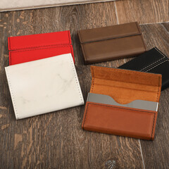 Colored leather business card holder, Genuine leather business card holder, concept shot, top view, different color, clamshell and stitched card holder. Dark wood background.