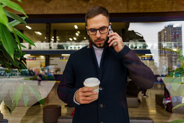 portrait of an attractive man wearing glasses and drinking coffee - talking on the phone, shot through the window