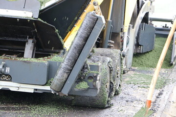 An industrial machine spreading and pressing green asphalt on a street