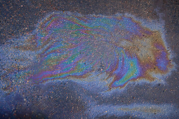 Colored texture of oil products on the asphalt in the rain.