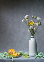 Still life with flowers. White, yellow wildflowers in a light tall vase on a light gray background,...