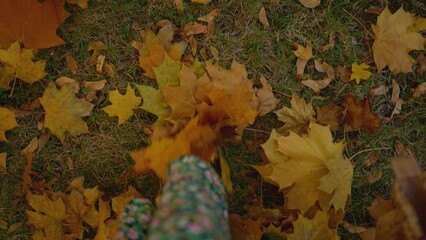 POV top view female legs in brown vintage leather elegant boots on yellow leaves background. first person view. woman relaxing in autumn city park at sunny fall day and kicks leaves