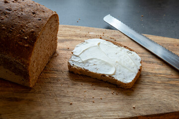 Slice of bread with mayonnaise spread on a wooden cutting board with bread next to it and a cutting knife - Powered by Adobe
