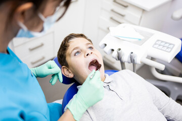 Unrecognizable woman dentist observes the teeth of a small child with a mirror. Treatment against...