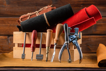 Leather pieces and leather craft work tools on the old wooden workbench background front view.
