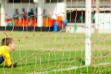Blurred young goalkeeper in the goal area, with goalpost net in focus