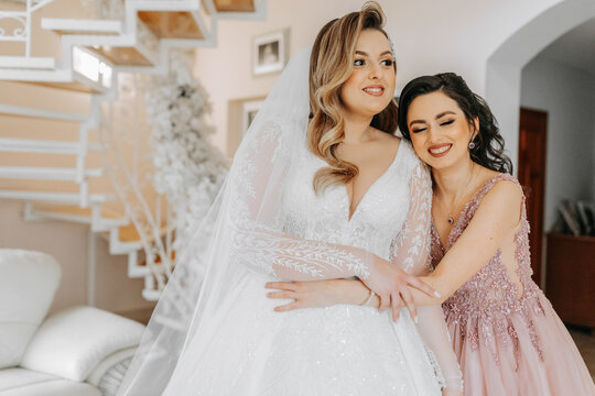 A friend helps the bride fasten her dress. A woman helps her friend fasten the buttons on the back of her wedding dress. The morning of the bride, the creation of a family, an important event.