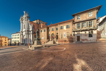 Fototapeta na wymiar Bra, Cuneo, Italy - The town hall and parish church Sant' Andrea Apostolo in Piazza Caduti per la Liberta, Coblestone with the statue of St. Joseph Cottolengo