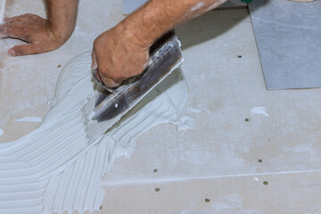 Tiler applying adhesive mortar cement plaster to floor for laying ceramic tiles