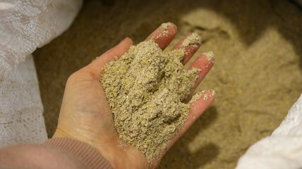 woman's hand holds a handful of crumbly non-granular feed over a bag, close-up, demonstration on the palm of a scattering of protein feed for birds and animals on a farm, organic feeding in livestock