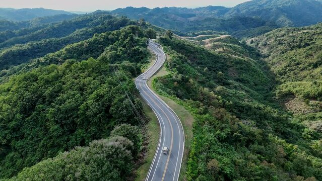 Aerial view highway Drone flying above winding road during sunlight, Winding asphalt road through tropical rainforest. countryside landscape. Landmark tourist attractions in Nan Province, Thailand.	