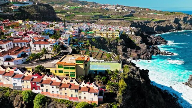 Aerial view of stone houses with red tiled roofs and delightful wooden balconies on the cliffs in Tenerife. View from above of colourful coastal La Laja natural pool in San Juan de la Rambla, Canary.
