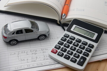 Close-up of a calculator next to a car and a notepad with notes on tax costs