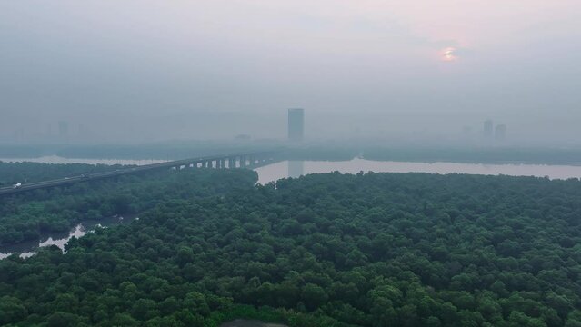 Dolly in drone shot over mangroves moving towards bridge over a river towards polluted hazy cityscape at sunrise in Mumbai, India. Easy morning view of outskirts of mumbai city by the riverside.