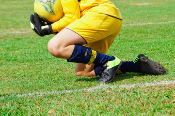 young soccer player goalkeeper defending the goal, holding the ball near the lawn