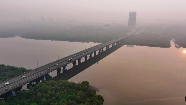 Aerial view of bridge with vehicles travelling on it at sunrise over a river or creek with poor air quality in Mumbai. Morning drone view of bridge over a river on a polluted morning.