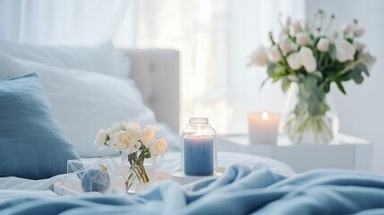 Cozy light white Bedroom with flowers and candles. pillows, duvet on a bed. Blue bed linen on a blue sofa. Bedroom with bed and bedding. Blurred view of light bedroom with big window