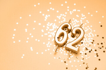 62 years celebration festive background made with golden candles in the form of number Sixty-two lying on sparkles. Universal holiday banner with copy space.