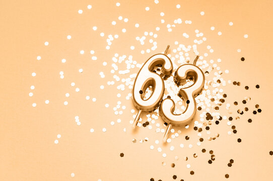 63 years celebration festive background made with golden candles in the form of number Sixty-three lying on sparkles. Universal holiday banner with copy space.