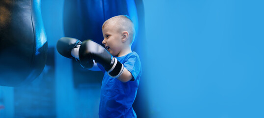 Portrait boy in black boxing gloves is training hit with punching bag. Banner sport kid boxer in gym, copy space