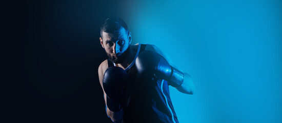 Male boxer trains punches on punching bag, dark background neon color. Concept banner sport boxing