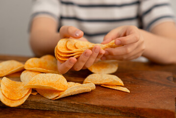 A child's hands engaging with potato chips, stacking them on a wooden table for a playful snack time.