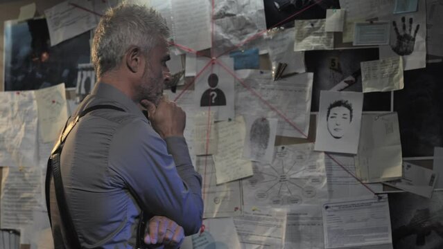 police detective sticks suspect killer identikit sketch on evidence board,pensive officer investigator working on the murder case