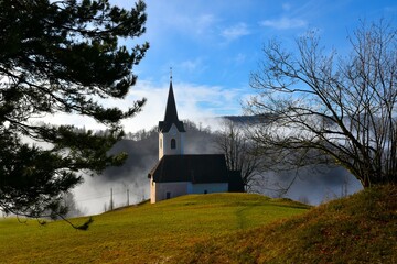 Fototapeta na wymiar Catholic church in Polhograjski Dolomiti hills with forest covered foggy hills