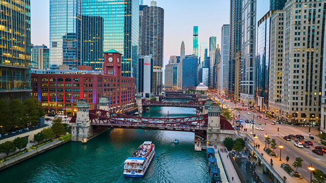 Chicago boat going under canal bridge aerial with city lights and skyscrapers at blue hour, tourism