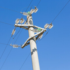 Concrete electricity pylon against a blue background with copper electrical cables and glass insulators